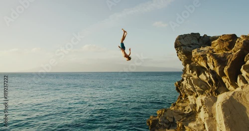 Young man doing backflip cliff jumping into ocean at sunset