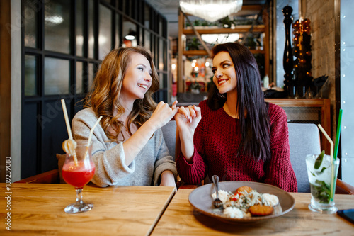 communication and friendship concept - smiling young women with nonalcoholic cocktails at cafe. two girlfriends blonde and brunette talk  joke and laugh