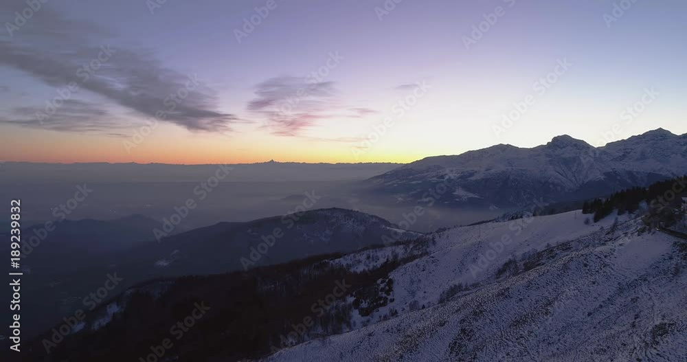 Backward aerial top view over winter snowy mountain with car travelling on road.Blue hour dusk or dawn twilight Alps mountains street path snow establisher.4k drone flight establishing shot Backward aerial top view over winter snowy mountain with car travelling on road.Blue hour dusk or dawn twilight Alps mountains street path snow establisher.4k drone flight establishing shot