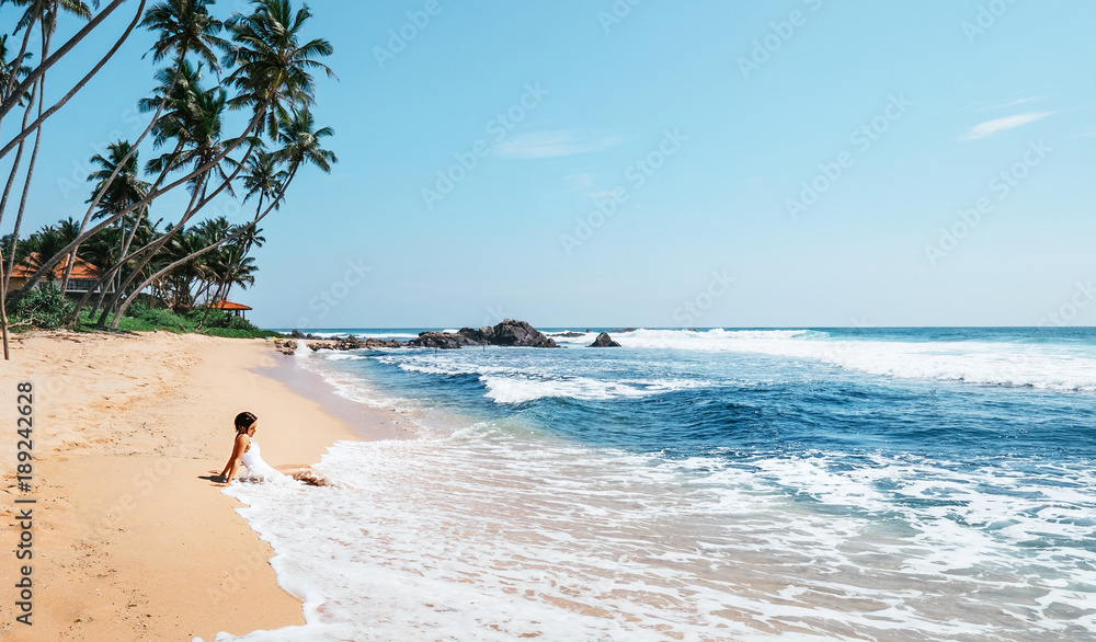 Woman enjoy with ocean surf sitting on the lonely tropical beach under the palm trees