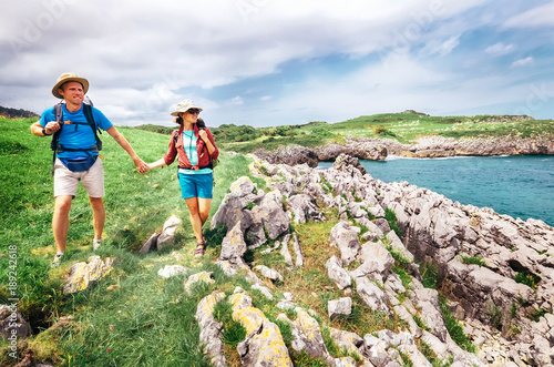 Couple backpacker travelers walk on ocean rocky coast. Asturias. Spain