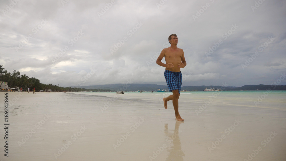 Man running along beach. Fitness sports runner man jogging on beach. Handsome young fit sporty male athlete running outside on beautiful beach training. Man running along beach. Fitness sports runner man jogging on beach. Handsome young fit sporty male athlete running outside on beautiful beach training.