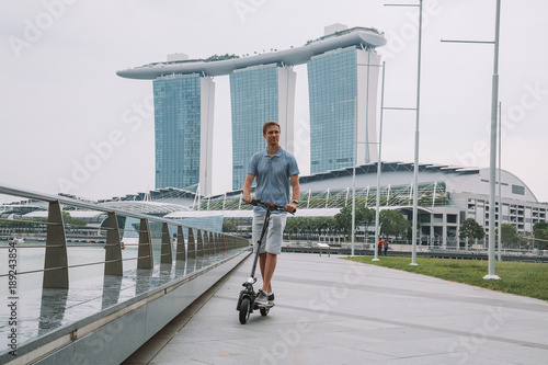 Photography Young man riding an electric scooter in Singapore with an amazing view on the city