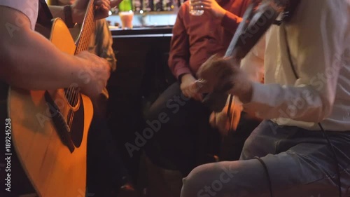 young people celebrate the day of St. Patrick. two men play the guitar and violin. live music in the bar. people are sitting on high taksoyah against the back of the bar. Holiday of drink and beer. 4