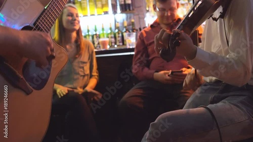 young people celebrate the day of St. Patrick. two men play the guitar and violin. live music in the bar. people are sitting on high taksoyah against the back of the bar. Holiday of drink and beer. 4