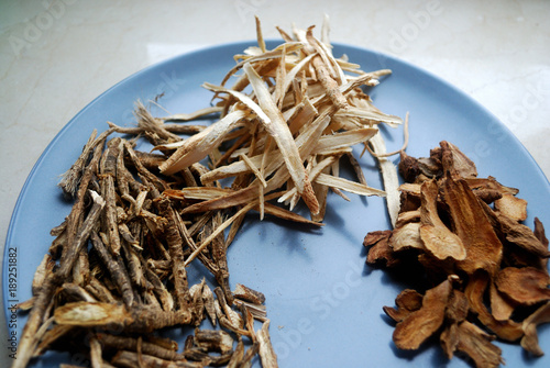 Assorted chinese traditional medicine herbs on a plate. Fang feng, bai zhu, huang qi roots sliced and dried. photo