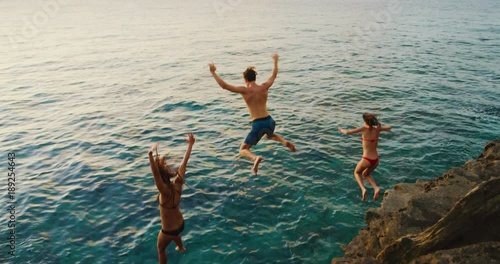 Friends cliff jumping into the ocean at sunset photo