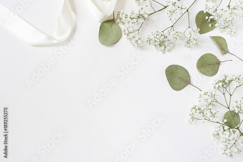 Styled stock photo. Feminine wedding desktop mockup with baby's breath Gypsophila flowers, dry green eucalyptus leaves, satin ribbon and white background. Empty space. Top view. Picture for blog. photo