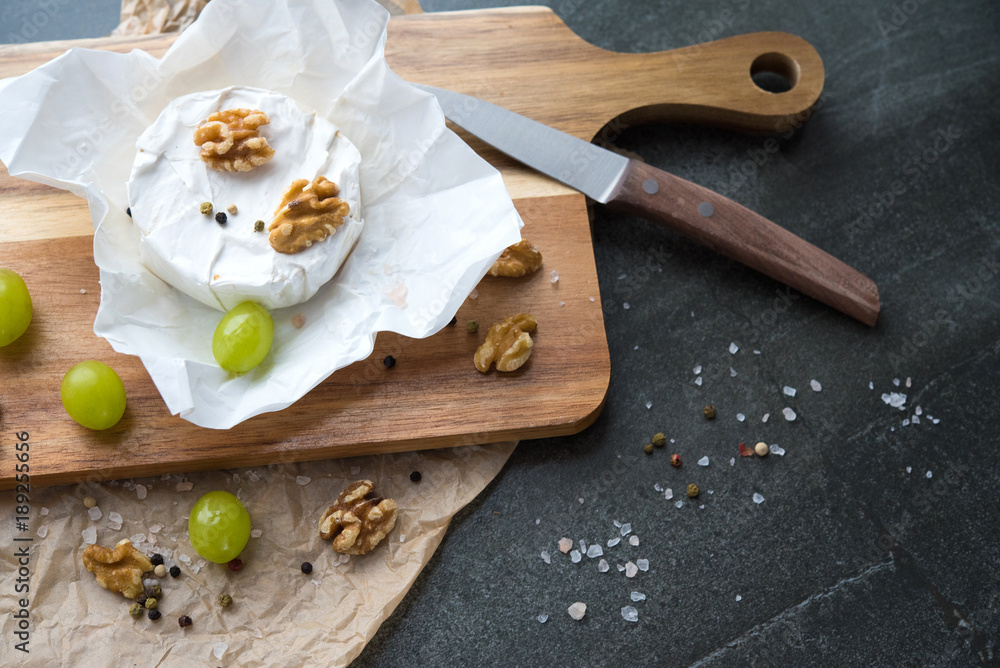 cheese camembert on a wooden board, decoration with nuts and grapes cheese camembert on a wooden board, decoration with nuts and grapes
