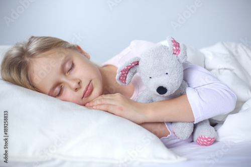 Child little girl sleeps in the bed with a toy teddy bear