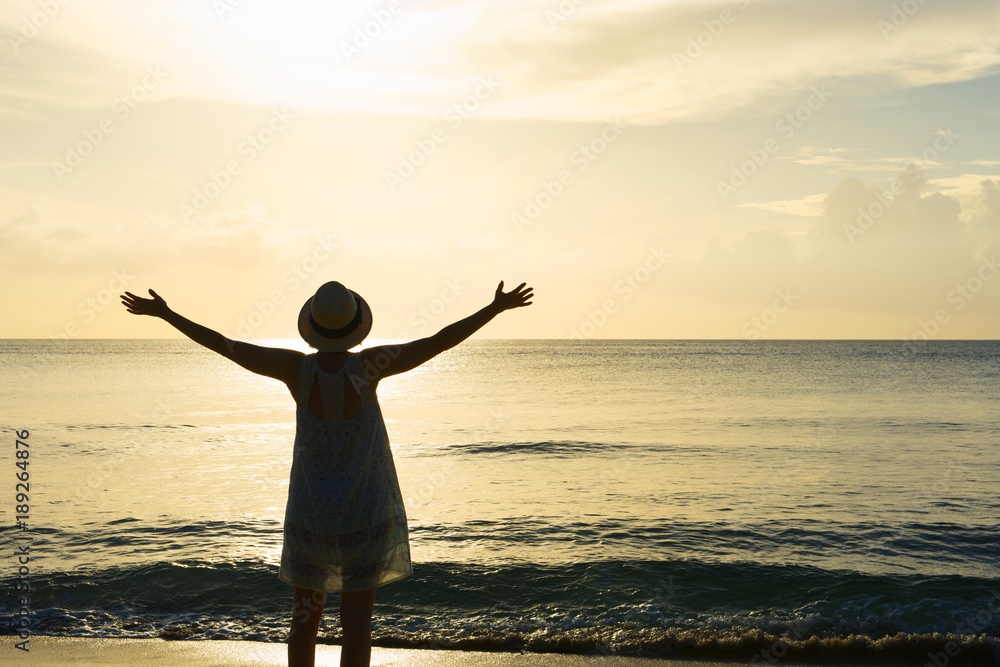 Fototapeta premium Silhouette of Woman, Arms Outstretched Facing Sunset on Beach