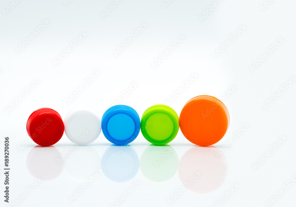Different size of white, green, red, blue and orange color round plastic screw caps in a line on white background and copy space. Different size of white, green, red, blue and orange color round plastic screw caps in a line on white background and copy space.