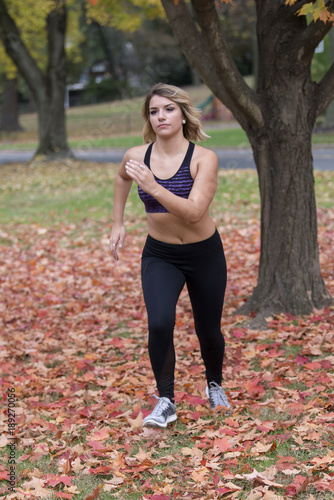 Sexy Caucasian female fitness runs outdoors in fall in purple sports bra and black leggings