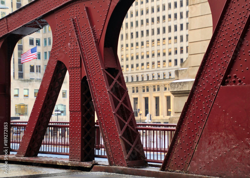 American Flag seen flying through design of street bridge in Chicago Loop during winter afternoon in January.