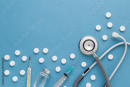 Medical equipment : stethoscope ampoules syringe White pills thermometer and stethoscope on blue background