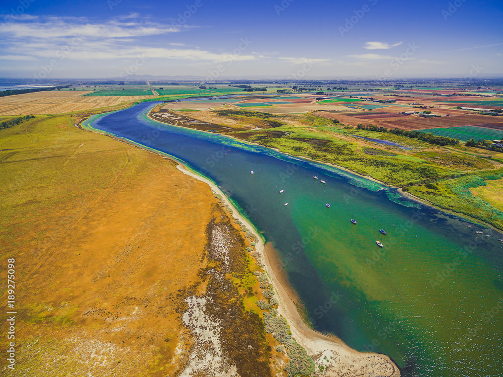 Aerial view of Werribee river with boats flowing among fields, meadows and pastures on bright summer day