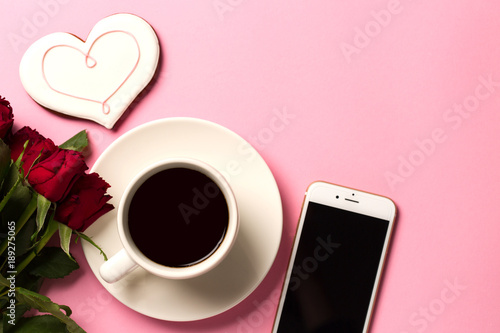 Morning valentine day concept background with roses, heart, smartphone and a cup of coffee. Top view with space for your text