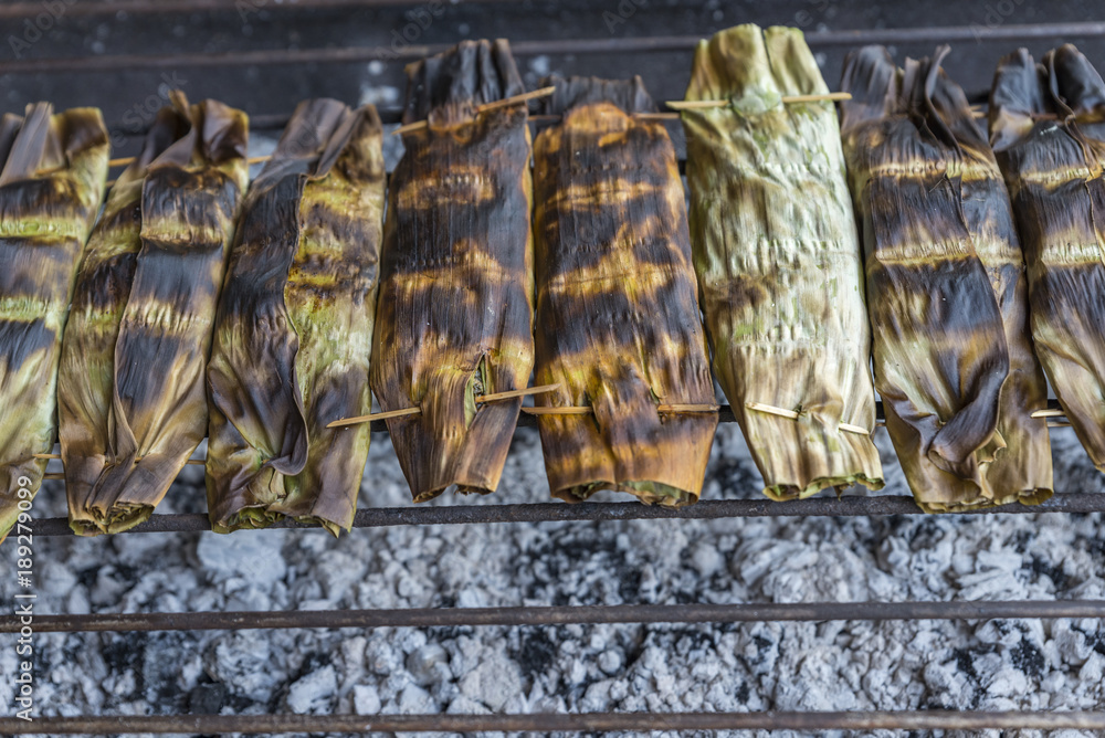 Sticky rice in banana leaf grill on charcoal at organic food market of Thailand. Close up pack of grilled sticky rice in banana leaf in a row. Space for text.