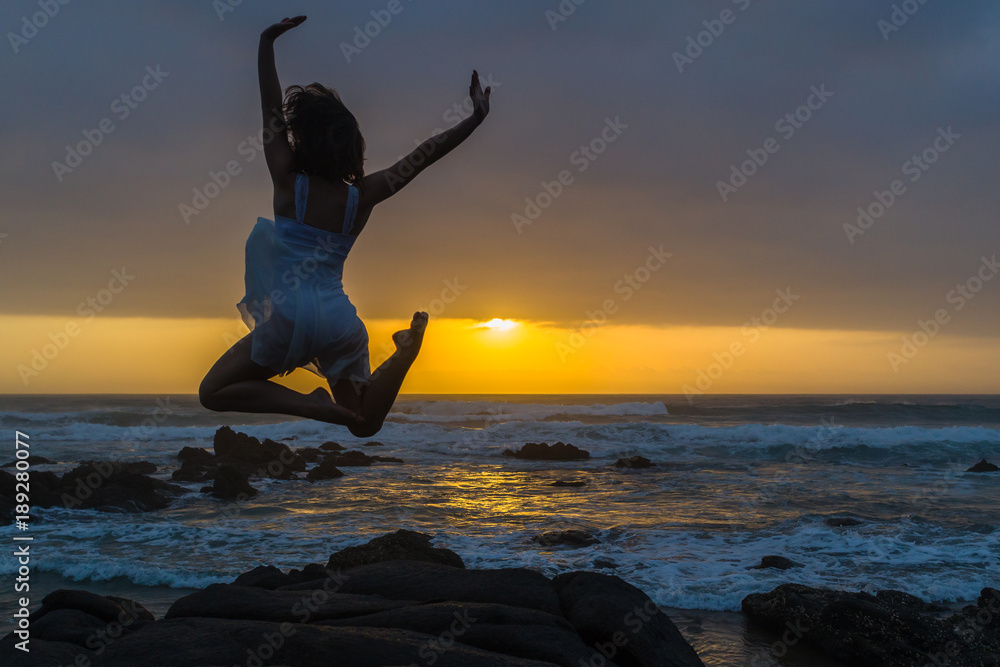 Young Girl Ballet Dancer on beach rocky coastline pose leap silhouetted dawn sunrise