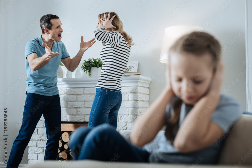 © zinkevych - Unhappy family. Unsmiling fair-haired little girl closing her ears and sitting on the sofa while her parents shouting at each other © zinkevych - Unhappy family. Unsmiling fair-haired little girl closing her ears and sitting on the sofa while her parents shouting at each other