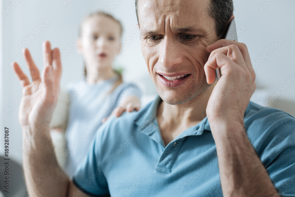 Silence. Busy concentrated dark-haired man talking on his phone and having no time on his daughter and she touching his on the shoulder Silence. Busy concentrated dark-haired man talking on his phone and having no time on his daughter and she touching his on the shoulder