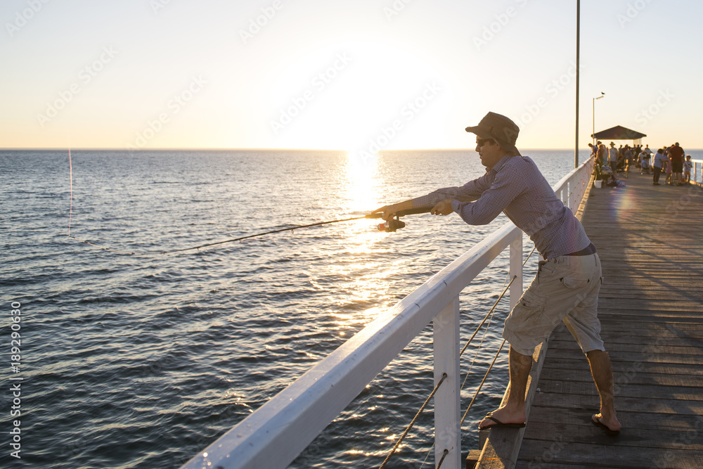 young attractive and happy man in shirt and hat fishing at beach sea dock using fish road enjoying weekend hobby in holidays