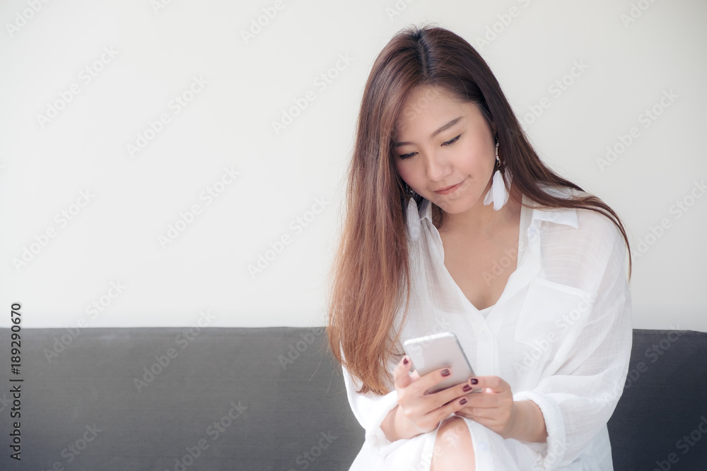 A beautiful Asian woman on white dress using and looking at a mobile phone with feeling happy and relaxed A beautiful Asian woman on white dress using and looking at a mobile phone with feeling happy and relaxed