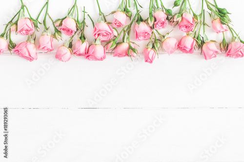 Flowers composition. Border made of pink rose flowers on white wooden background. Flat lay, top view, copy space