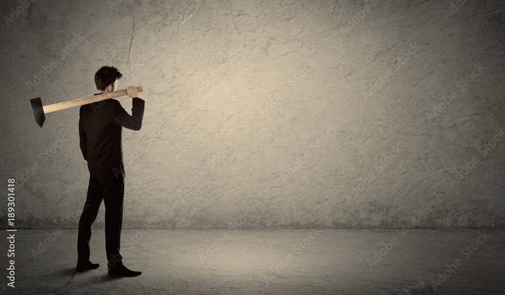 Business man standing in front of a grungy wall with a hammer Business man standing in front of a grungy wall with a hammer