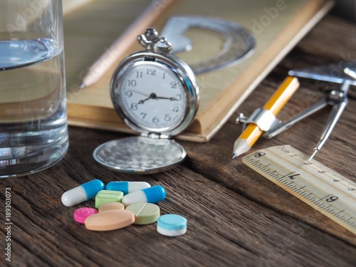 Time to take medicine. Pocket watch, Colorful medicine, water glasses, stationery and stationery. On the old wood table, meaning do not work until you forget to take medicine.