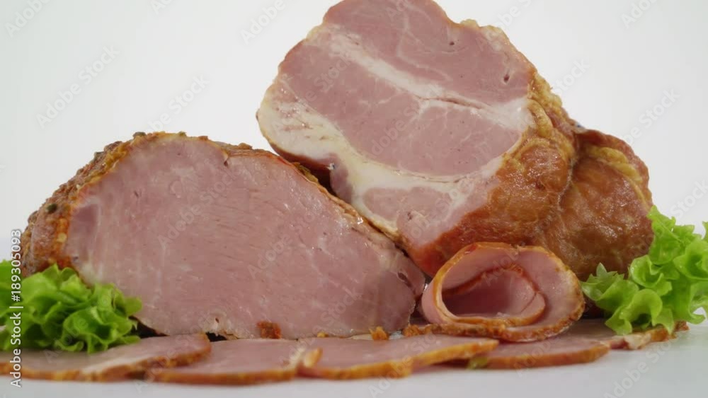 Dolly: Sliced processed meat products on white background. Smoked pork bacon with slices and herbs closeup. Dolly: Sliced processed meat products on white background. Smoked pork bacon with slices and herbs closeup.