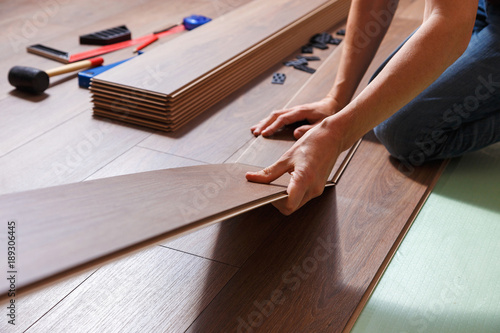 Male hands installing wooden laminate flooring. On the floor are different carpenter's tools.