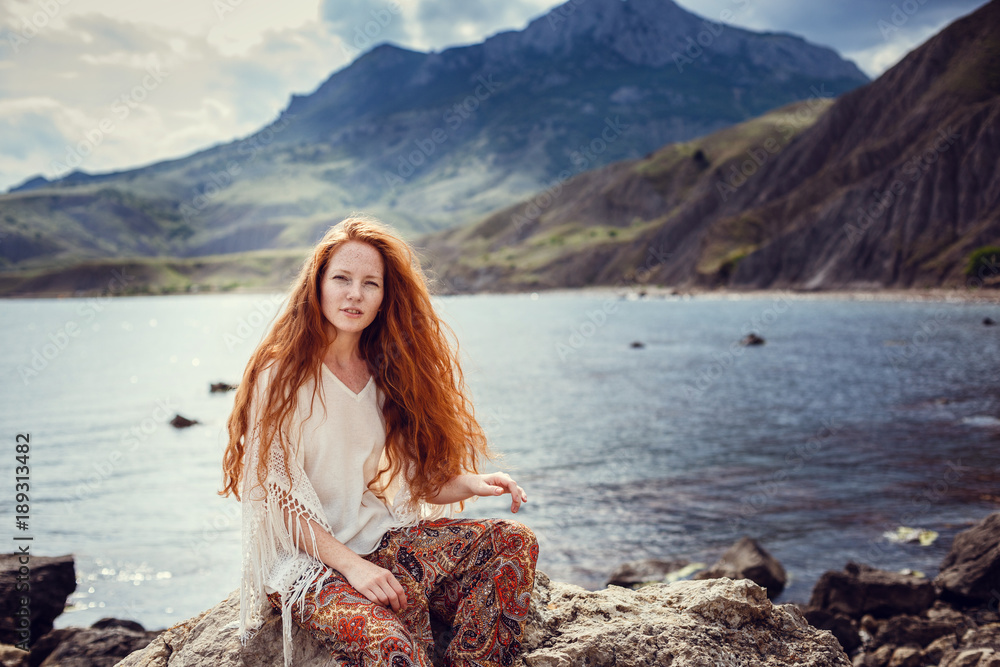 Young red-haired girl in the style of Boho. Enjoys the beauty of the sea coast. The idea and concept of freedom and hippies