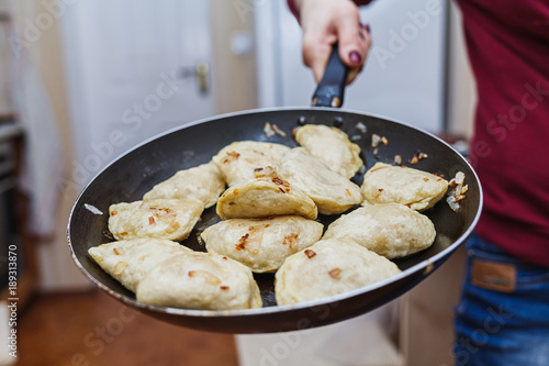 A women hand with Ukrainian traditional dish with boiled dough with onion fries on a frying pan. Closeup view.
