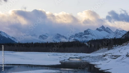 Time lapse of clouds flowing over snowy mountain peaks at sunrise