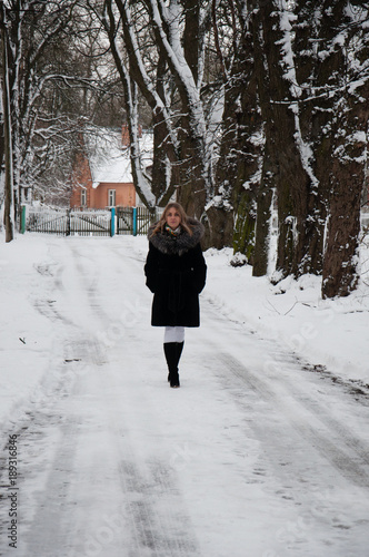 A woman is walking along a snow-covered alley in the park