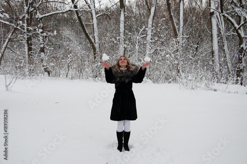 Joyful girl in a black coat playing snowballs in a winter forest