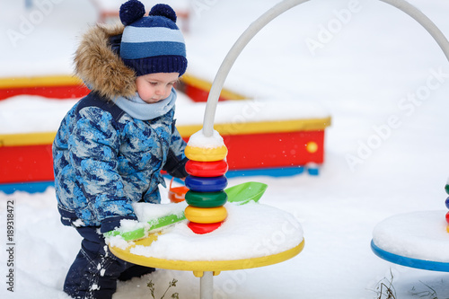 Мальчик играет на заснеженной детской площадке