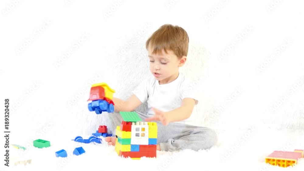 Little boy building a toy house of colored blocks sitting on a white background. Child and toys. Little boy building a toy house of colored blocks sitting on a white background. Child and toys.