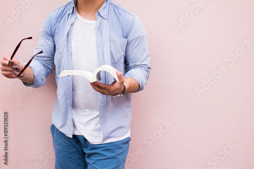 Asian man handsome  in blue shirt  holding  black glasses .Man standing on pink background oudside reading book and relaxing. Selective Focus. photo