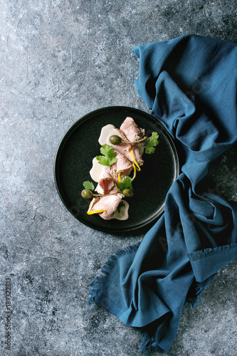 Vitello tonnato italian dish. Thin sliced veal with tuna sauce, capers and coriander served on black plate with blue textile over blue texture background. Top view, copy space photo