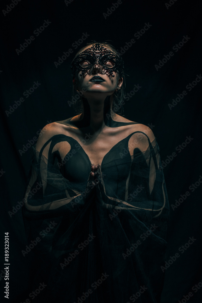 Beautiful young girl stands in transparent shawl with painted body and black mask. Body art.