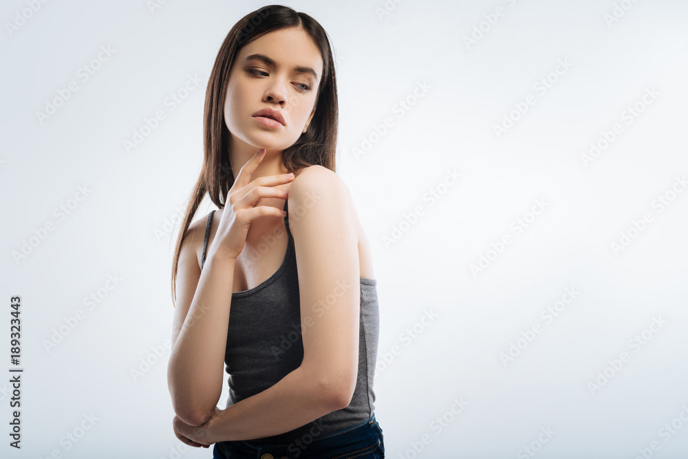Self secured. Beautiful focused pleasant woman posing on the isolated background while touching her chin and looking aside Self secured. Beautiful focused pleasant woman posing on the isolated background while touching her chin and looking aside