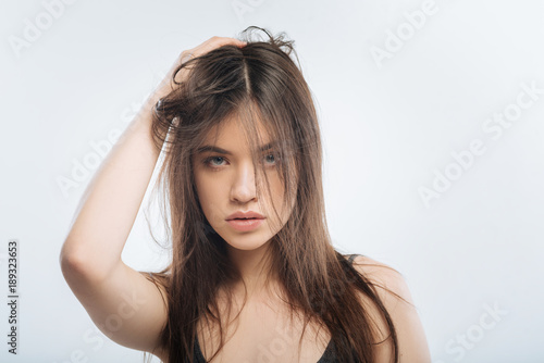 Family quarrel. Attractive smart carefree woman posing on the light background while touching her hair and staring at the camera