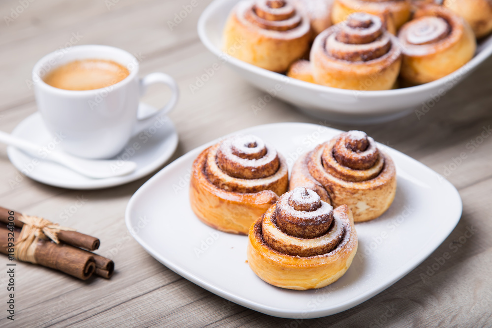 Fresh homemade buns with cinnamon, a cup of coffee, cinnamon sticks. Selective focus, close-up Fresh homemade buns with cinnamon, a cup of coffee, cinnamon sticks. Selective focus, close-up
