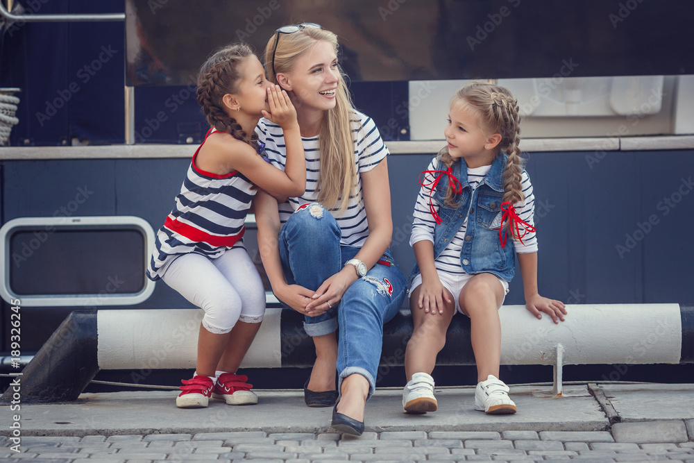 Obraz premium The elder sister and younger sisters and a brother in a marine style against the backdrop of boats and yachts. Idea and concept Friendship, vacation, vacation, family