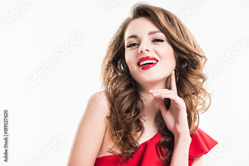 smiling attractive girl with makeup and red lips touching face with hand isolated on white