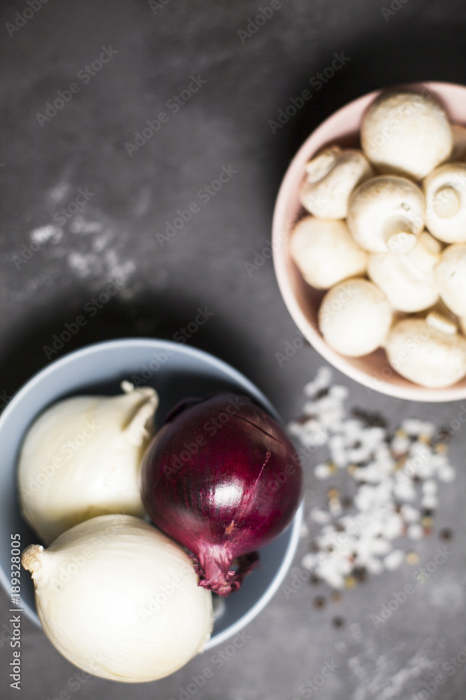 Diet, Italian Food Cooking, Vegetarian Concept. Bowls with fresh button mushrooms and red and white onions, sea salt grains and black pepper corns on a dark concrete background, top view Diet, Italian Food Cooking, Vegetarian Concept. Bowls with fresh button mushrooms and red and white onions, sea salt grains and black pepper corns on a dark concrete background, top view