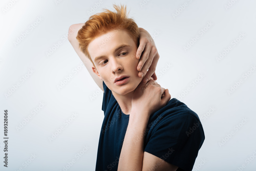 Fototapeta premium Innocent look. Appealing cute nice guy placing hands on the neck and looking aside while dressing in t shirt 