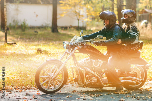 Fototapeta Naklejka Na Ścianę i Meble -  Young romantic couple in a forest road on a motorcycle. Love, freedom, togetherness concept. Happy guy and girl travel on a motorbike, road trip adventure concept